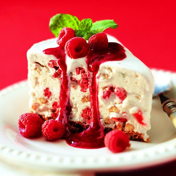 A slice of ice cream fruitcake drizzled with sherried berry sauce, on a white plate.