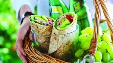 Two pieces of avocado tuna wrap in a basket with grapes and two bottles of sparkling water