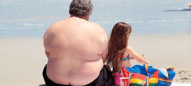 obese man with little girl on beach, ocean water
