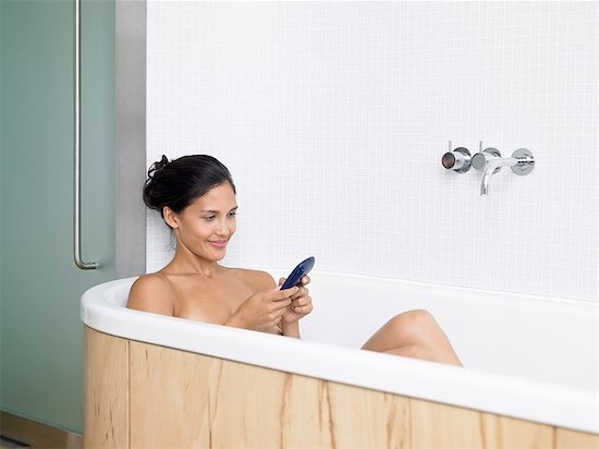 woman in bathtub texting on phone