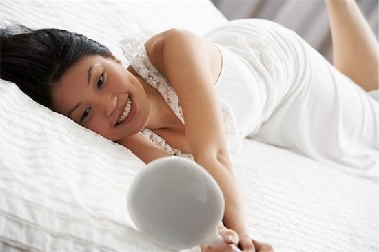 asian woman looking at mirror in bed