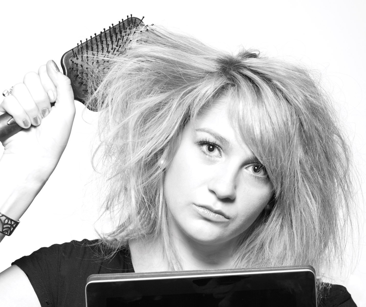 Black-and-white photo of girl with frizzy hair and paddle hair brush, frowing face, bad hair day