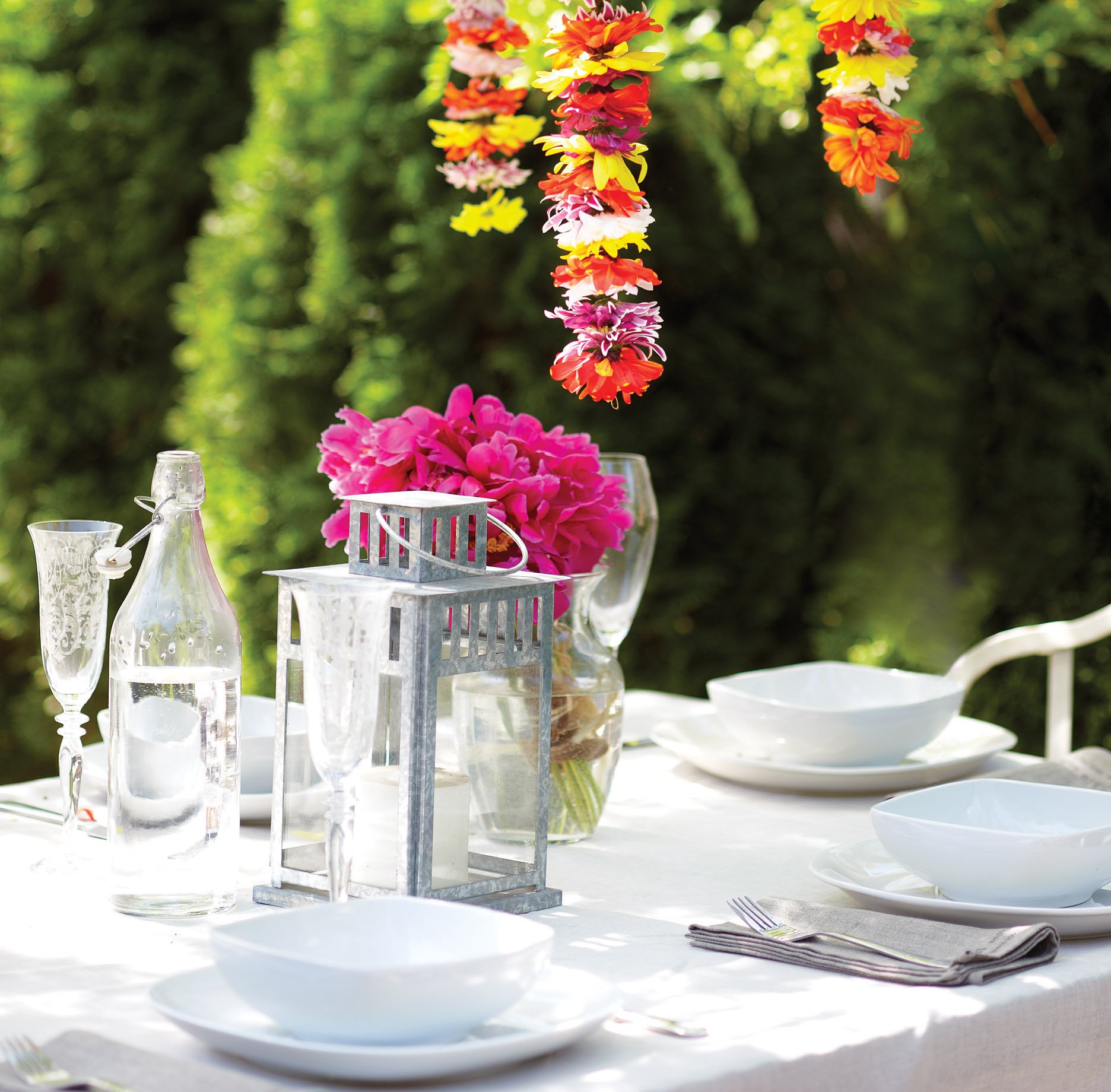 Outdoor table with hanging flowers, white dishware, champagne flutes, flower garlands, backyard party, dinner party