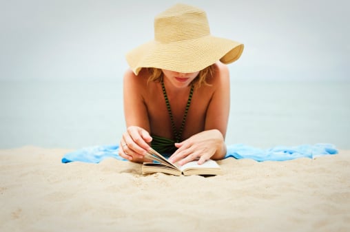 woman wearing summer hat on beach reading book