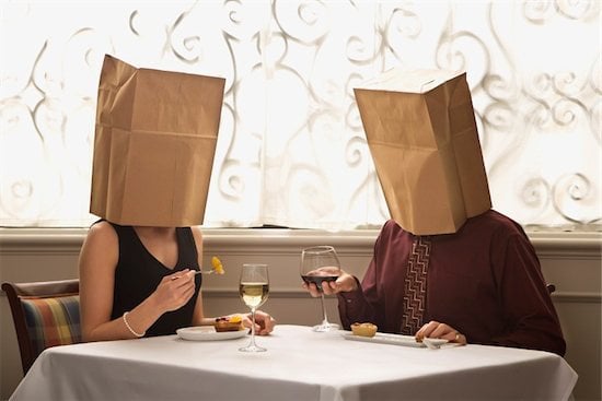 Two people sit at dinner with bags on their heads, blind date