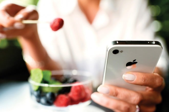 Woman eating fruits dessert with iPhone 4s in hands