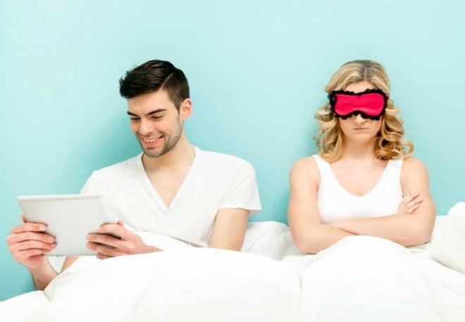 Couple in bed. Wife angry, husband absorbed with his digital tablet.