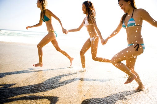 Three women holding hands and running on the beach