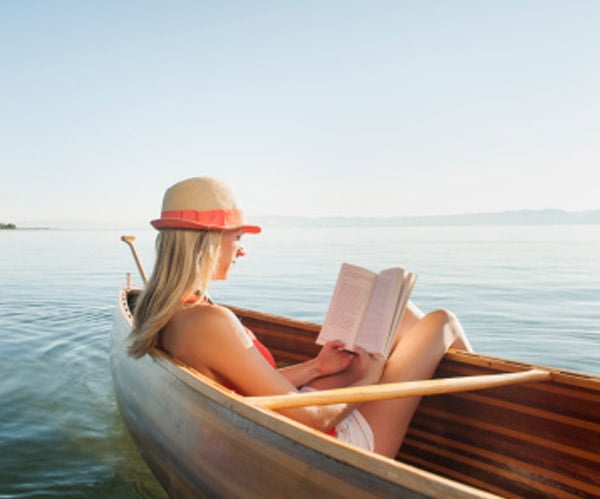 blonde woman wearing hat in canoe reading summer lake