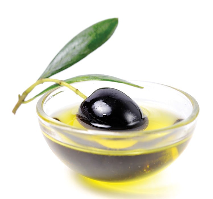 A black olive sits in a bowl of olive oil