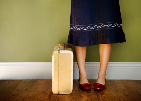 A woman stands alone with her suitcase packed