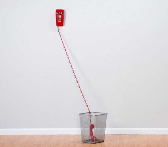 A red phone sits off the hook in a waste paper basket