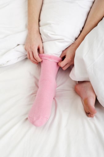 woman puts on socks in bed