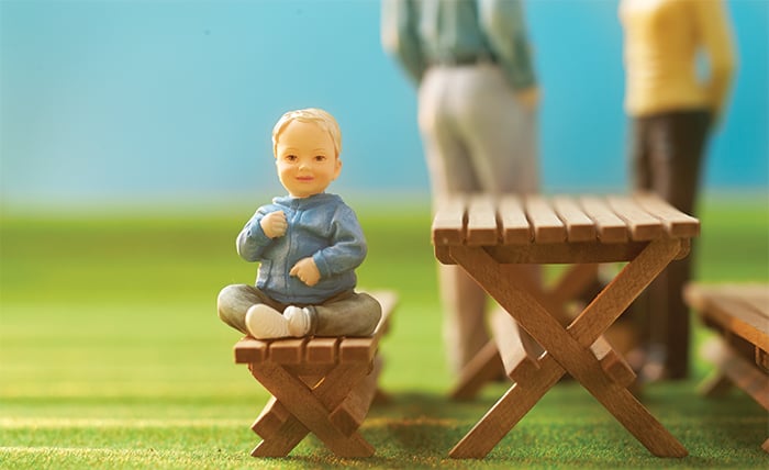 Miniature baby figurine with parents, mother and father, in the background.