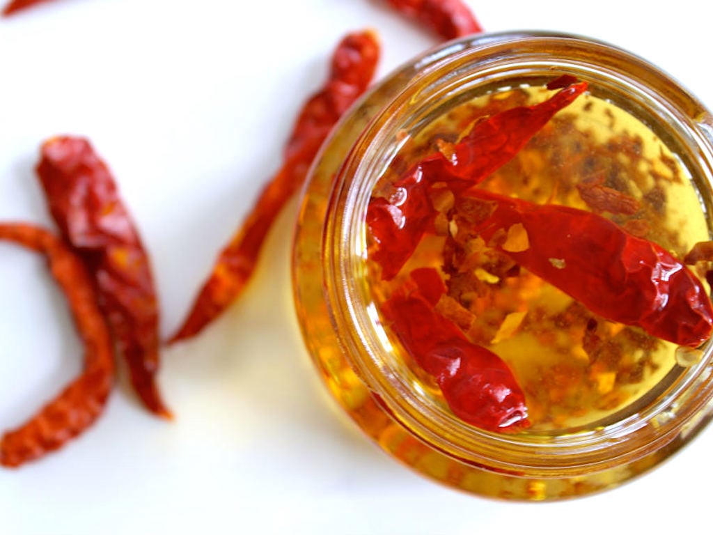 A clear jar that has oil with dried chilis and dried chili flakes in it.