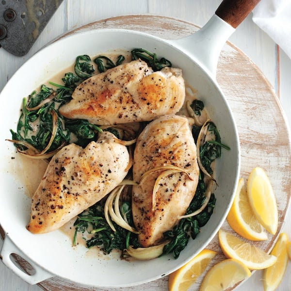 Lemon-garlic chicken with spinach in a skillet on a wooden serving board
