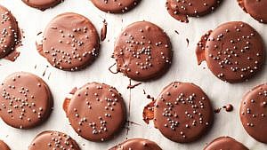 Chocolate-Mint Cookie Thins, drizzled with chocolate and silver dragées, on parchment paper