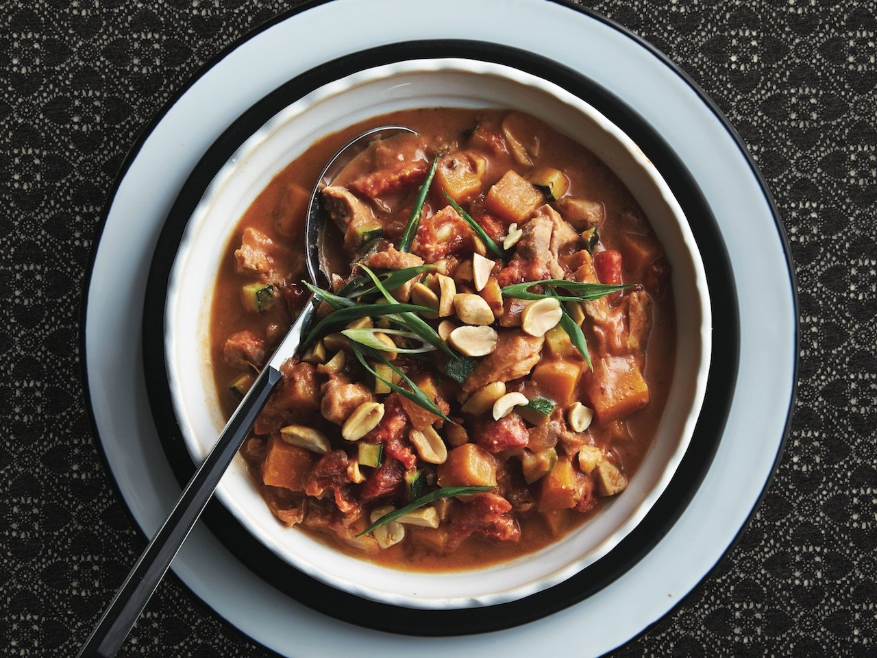 A bowl with chicken, nuts, and squash.