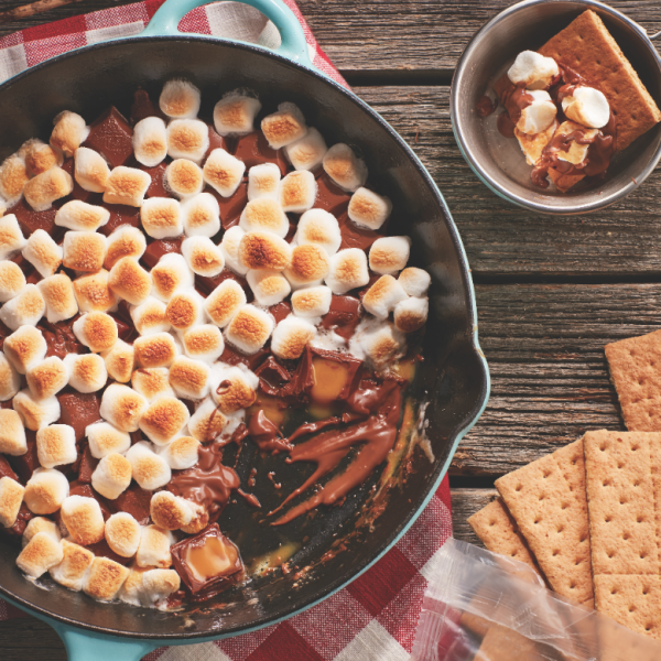 Caramel skillet s'mores recipe: one pan of s'mores on a picnic table with graham crackers on the side
