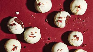 White And Dark Chocolate Pink Salt-And-Pepper Whiskey Truffles one with bite out of it on a red background