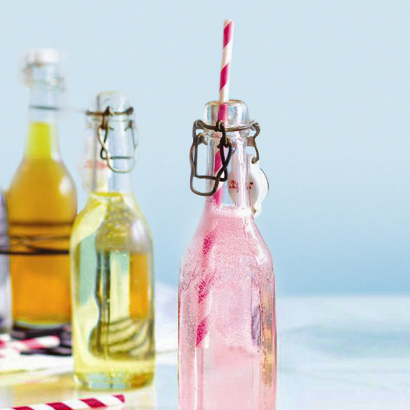 Pink Rhubarb syrup pop in a bottle with a red and white striped straw beside other bottles of syrup
