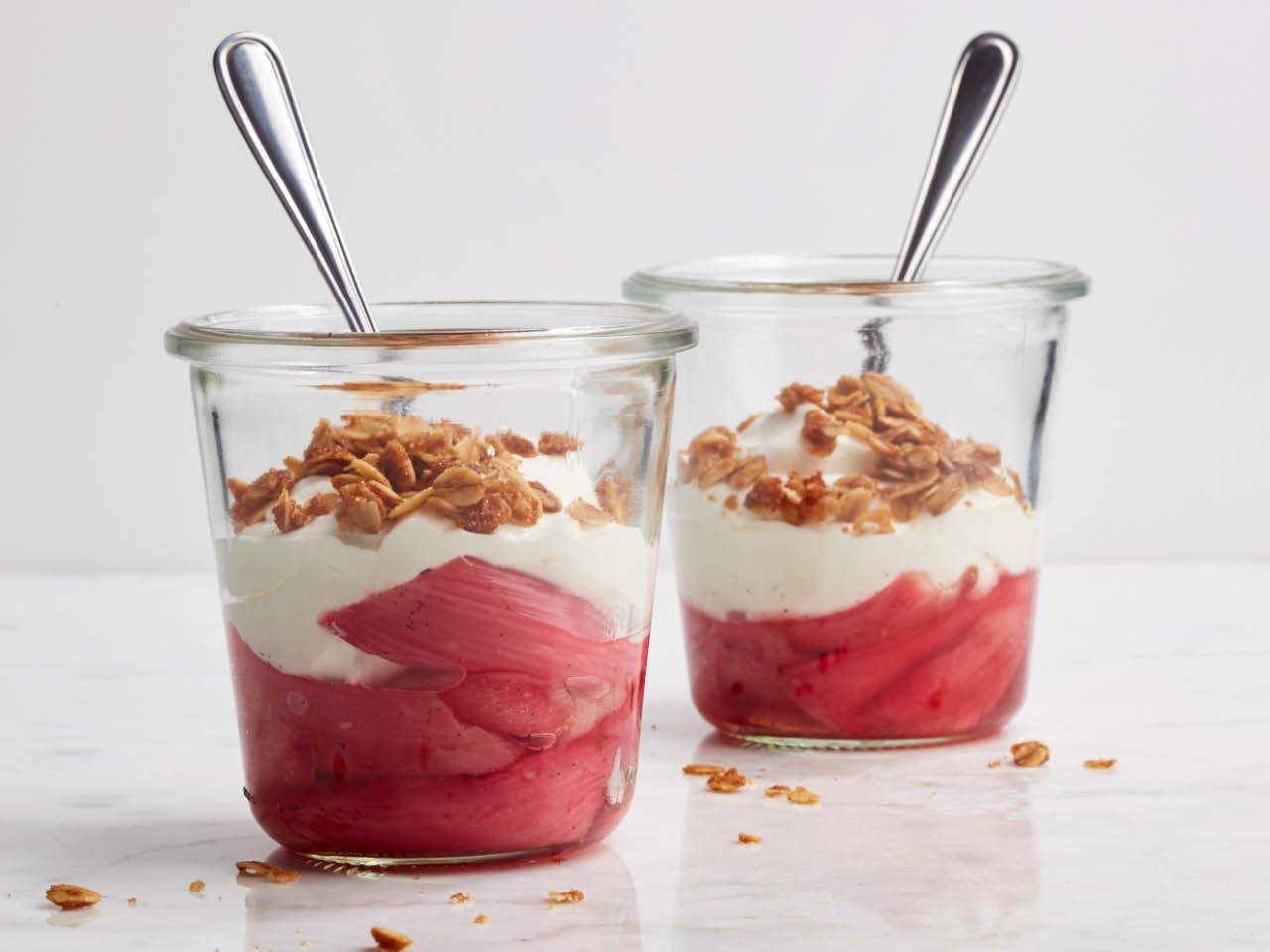 Rhubarb cranachan in a glass with a spoon stuck into and another glass of the same desert behind it on a white counter with crumbs