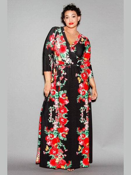 A woman with short, brown, curly hair wears a full-length black-and-red floral wrap dress with three-quarter-length sleeves from Sexy Plus Clothing.