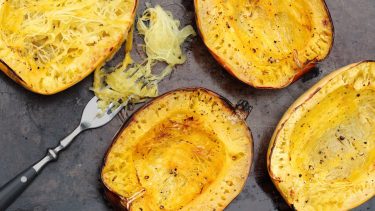 How to roast spaghetti squash: halves of roasted squash on a tray with a fork