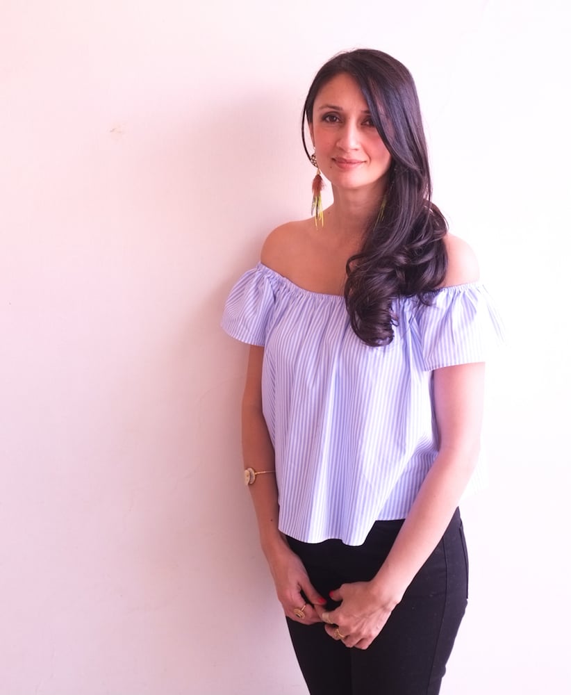 Shayma Saadat in a pink off the shoulder short and black pants in front of a light rose-coloured background
