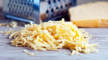 Pile of shredded cheese in front of box grater