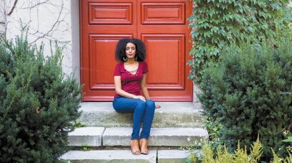 Black Foodie founder Eden Hagos sits on stone steps in front of a red door