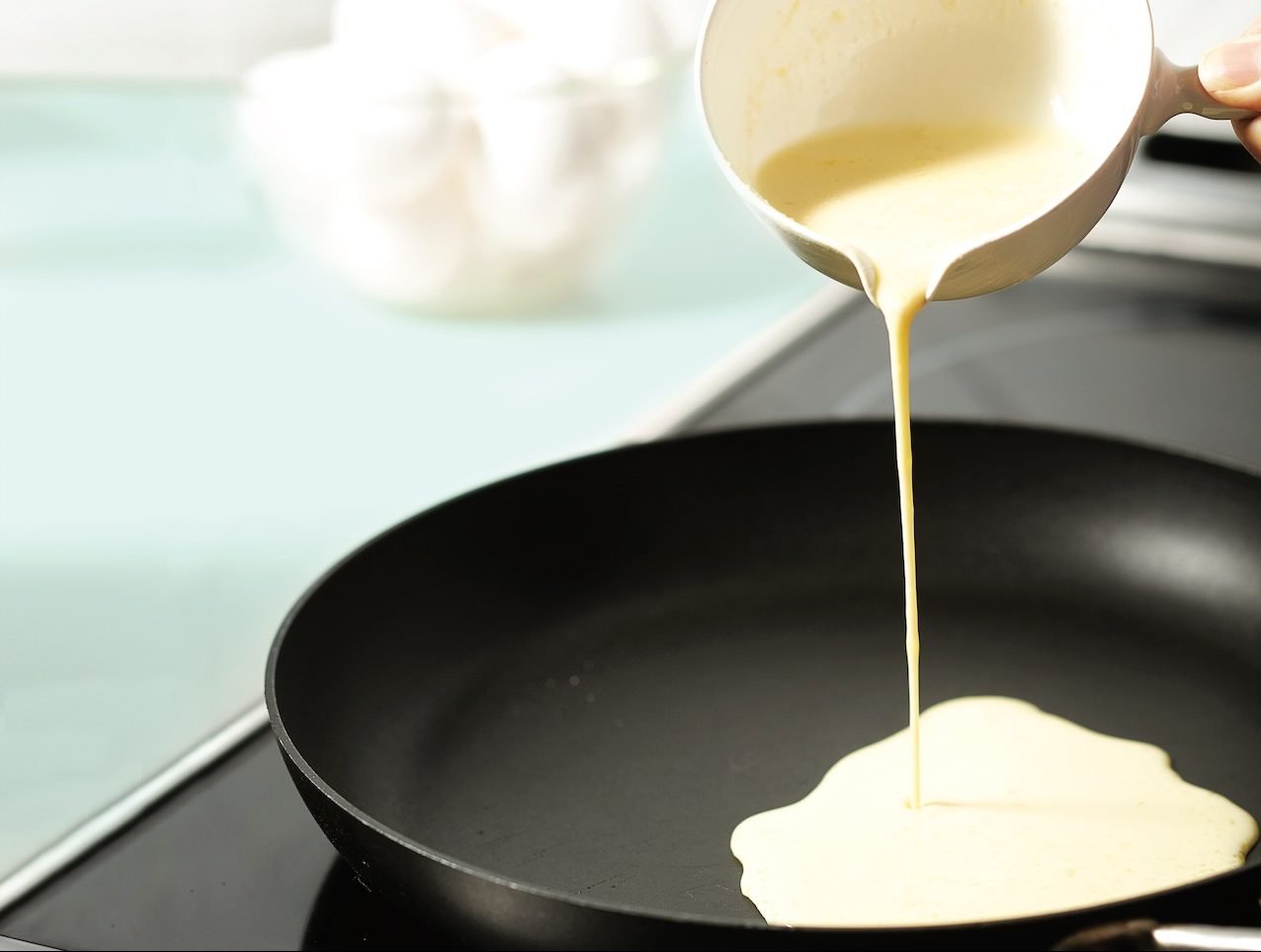 How to make crepes: Measuring cup of crepe batter pouring into a frying pan