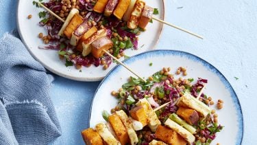 Halloumi and sweet potato skewers served on lentil salad on a blue table