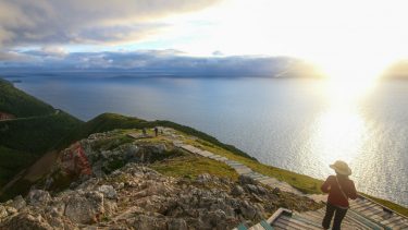best nature spot cape breton highlands visitor in hat gazes at sunset from stairs on grassy hill