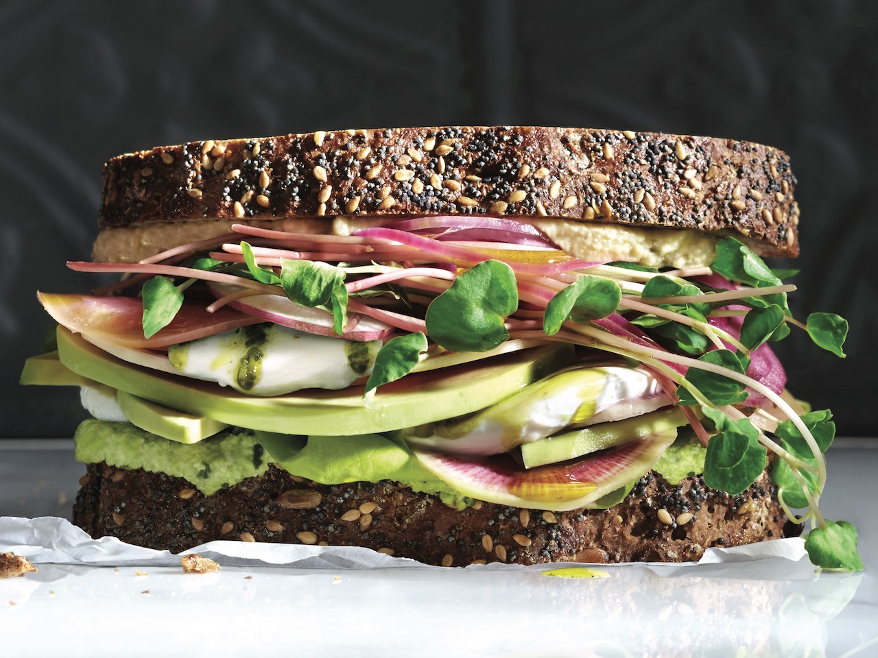 A superfood sandwich with avocado, lettuce, beets, and hummus layered between two slices of grainy bread