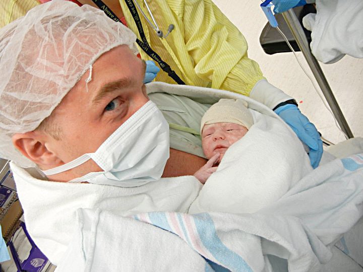 opioid addiction stigma-a man in a hospital mask holds his newborn baby