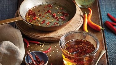 Hot red chili oil in pan and in a separate jar with different whole chilies scattered around.