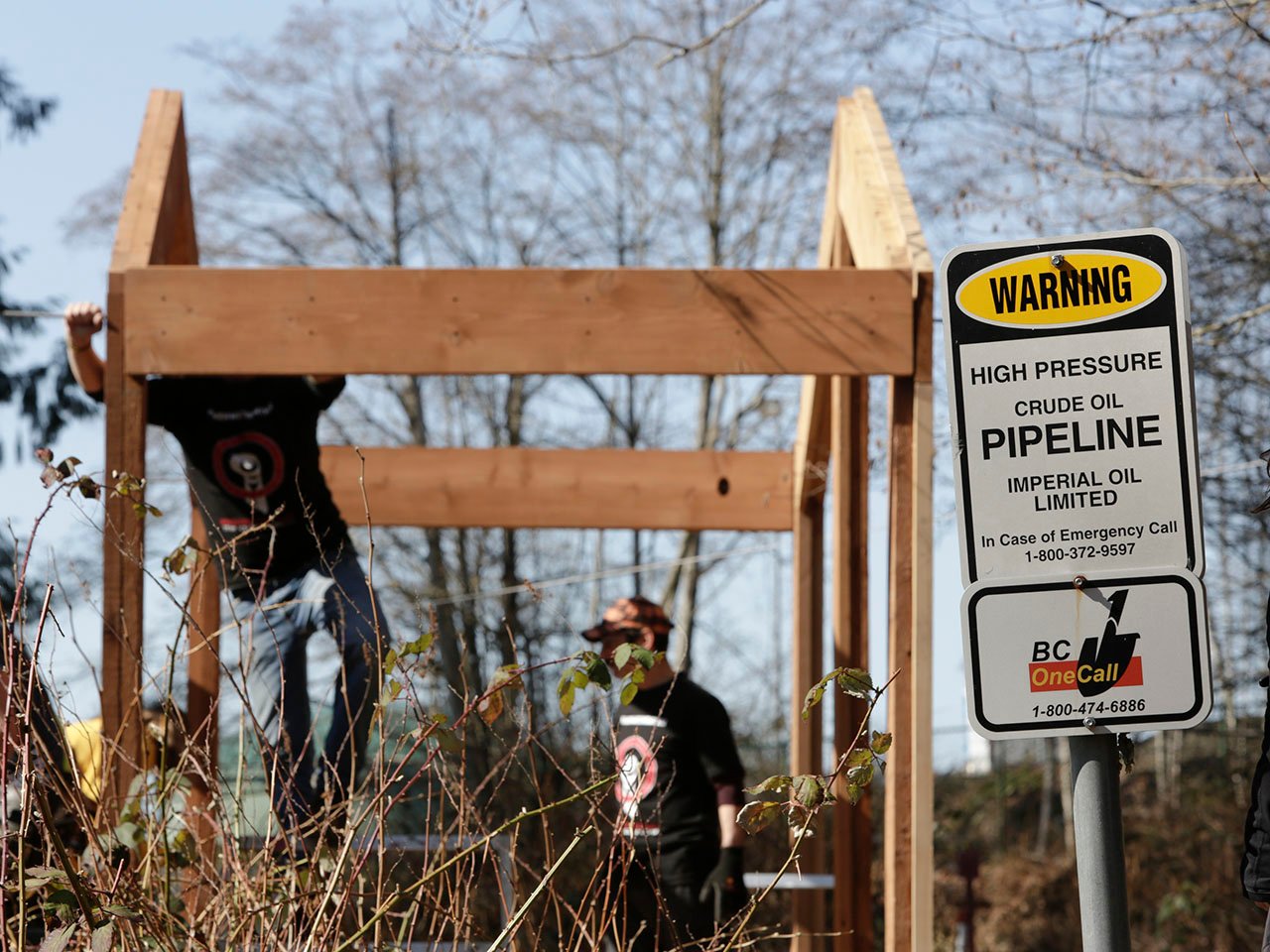 Everything you need to know about pipelines in Canada: Two people build structure behind a crude oil pipeline warning sign