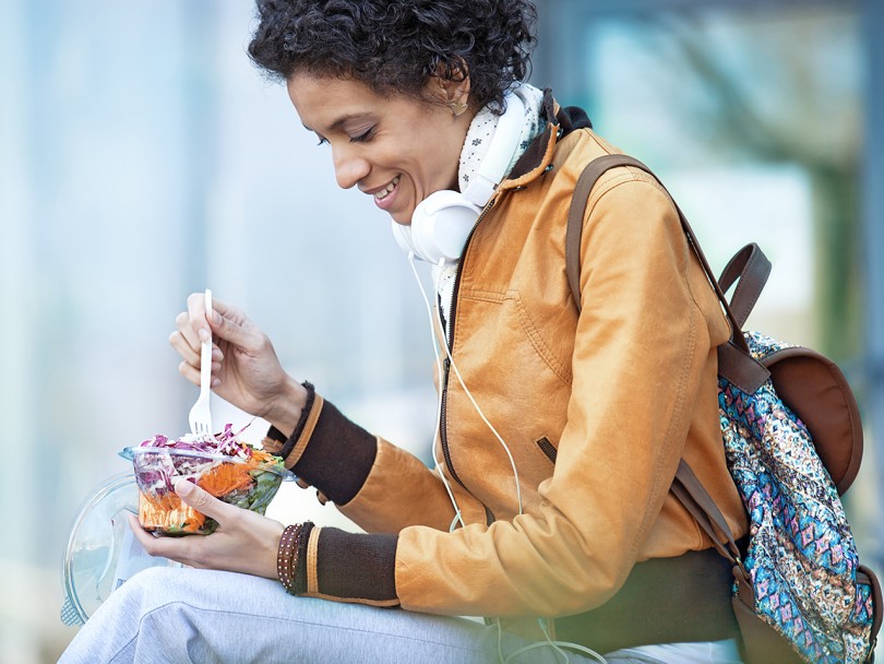Woman with headphones and backpack eats lunch outside: What is self-care?