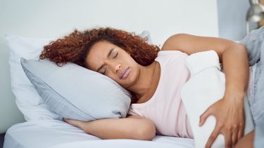 woman lying down with hot water bottle — ways to survive perimenopause