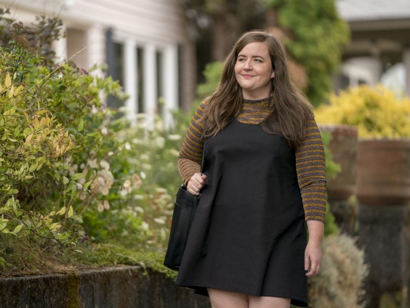 Aidy Bryant as Annie in her new TV show Shrill, walking down a tree-lined street in a black dress.