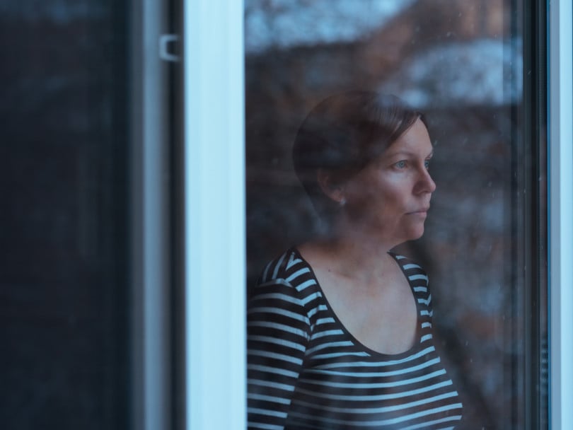 Eco-anxiety stressed and depressed woman standing by the window looking out at rainy weather