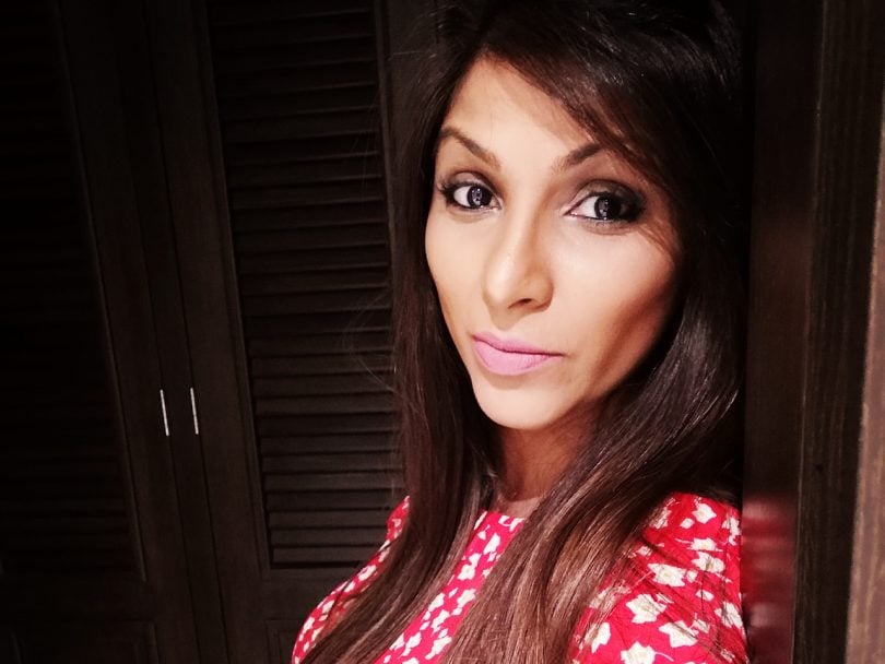 Epilepsy essay-Meera Solanki Estrada poses for a selfie in a red shirt against a dark background