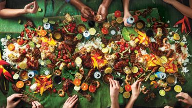 A table of friends digs into a table of Filipino food — a kamayan feast — including grilled adobo kalbi ribs and fried garlic rice