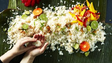 overhead shot of a pile of fried rice on a leafy green background, garnished with garlic, limes, and green onion