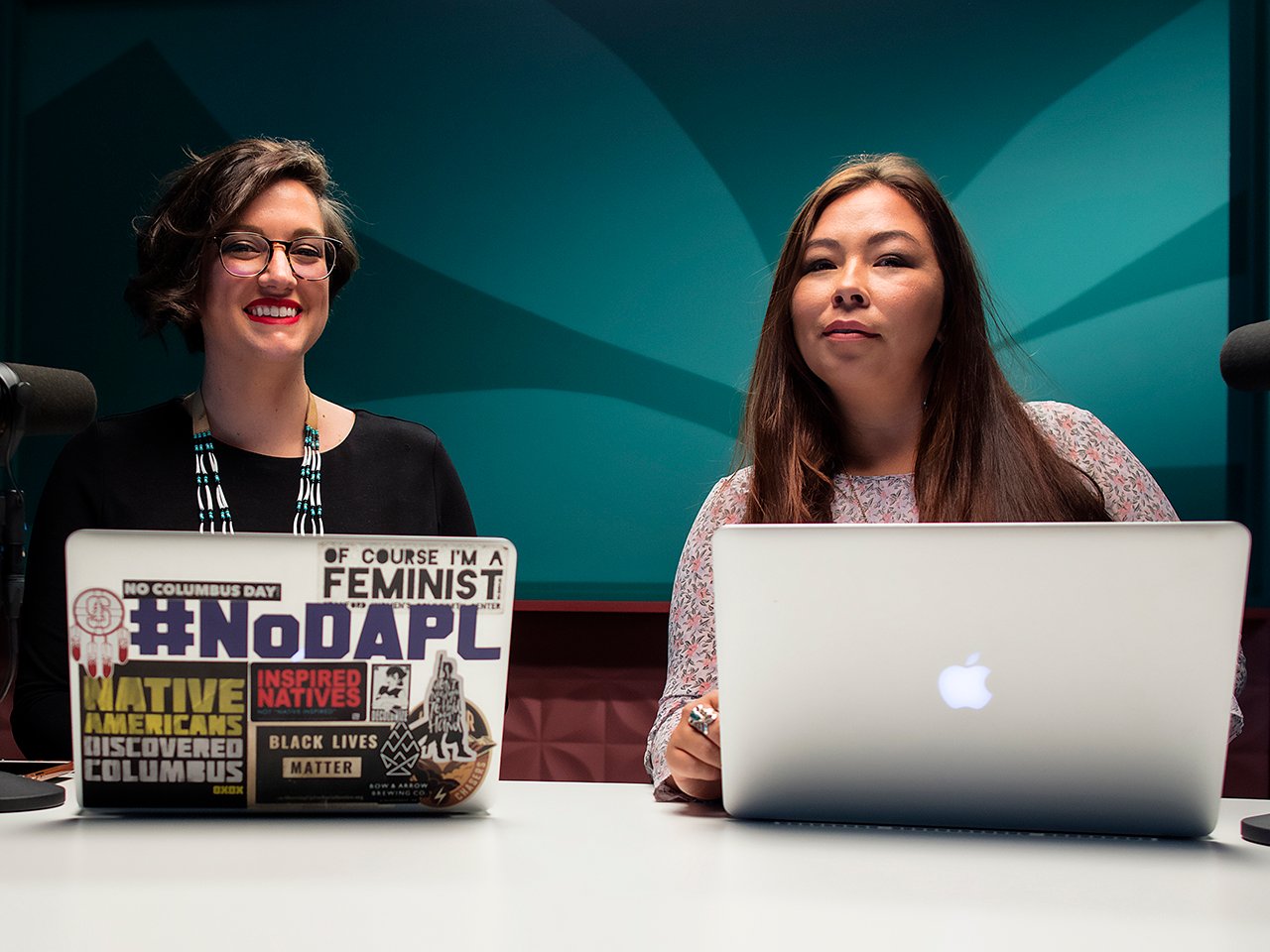 Indigenous podcasts: All My Relations hosts Adrienne Keene with laptop with stickers and Marika Wilbur with Mac laptop