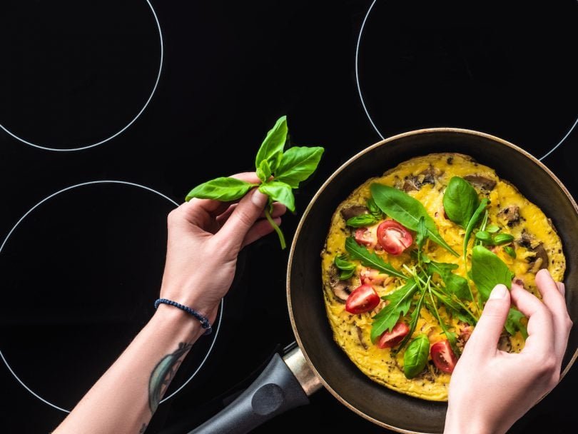 cropped shot of woman cooking omelette in frying pan on black induction cooktop
