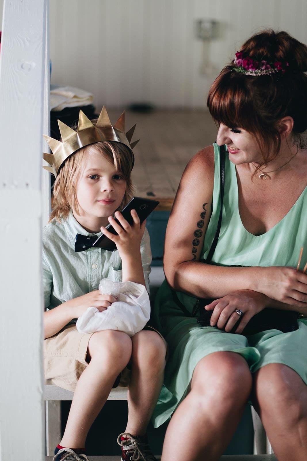 The author wearing a mint green dress sits with her son who is wearing a mint green shirt, bow-tie and golden paper crown in a current-day photo