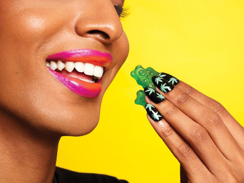 A person eats a CBD gummy with marijuana-painted manicure