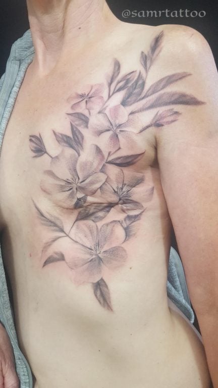 A woman's chest with floral grey and black tattoos covering mastectomy scars